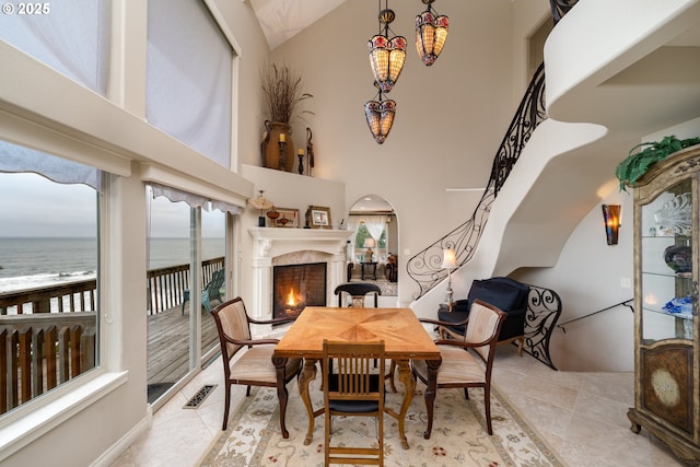 dining area with a water view, light tile patterned floors, and high vaulted ceiling