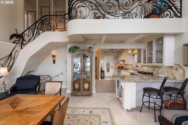 kitchen with tasteful backsplash, a notable chandelier, light stone counters, kitchen peninsula, and wall chimney range hood