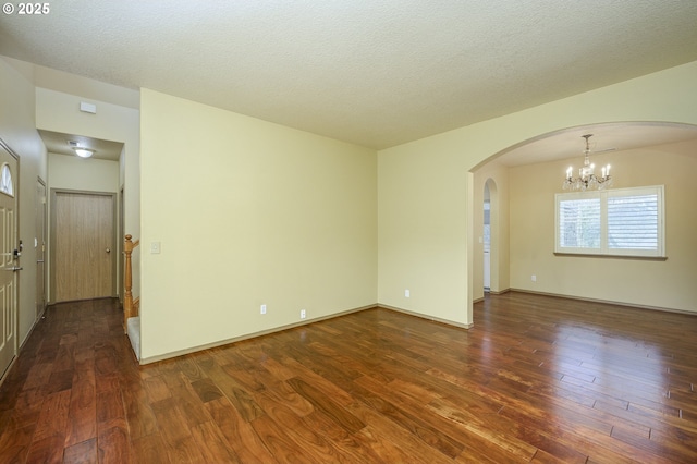 unfurnished room featuring a textured ceiling, arched walkways, dark wood-style flooring, baseboards, and a notable chandelier