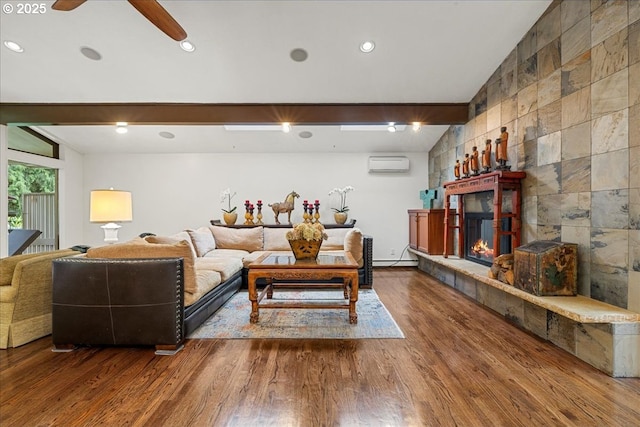 living room with wood finished floors, a wall mounted AC, a tiled fireplace, and a ceiling fan