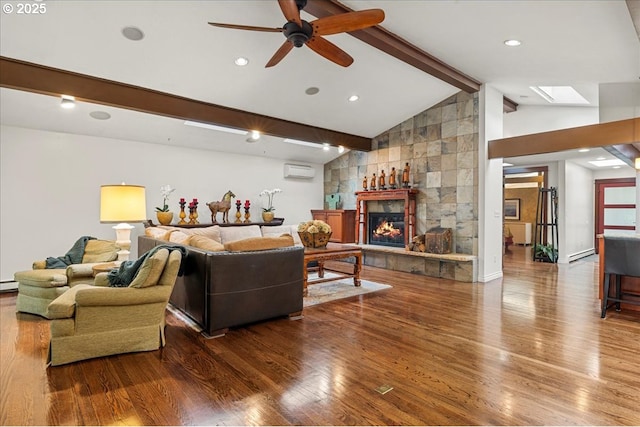living room with a skylight, a wall mounted air conditioner, wood finished floors, a glass covered fireplace, and ceiling fan