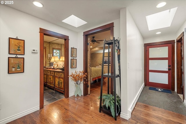 hallway featuring a skylight, wood finished floors, recessed lighting, and baseboards