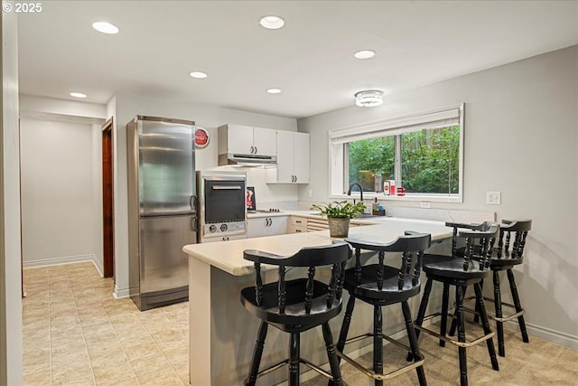 kitchen with freestanding refrigerator, a peninsula, oven, light countertops, and recessed lighting