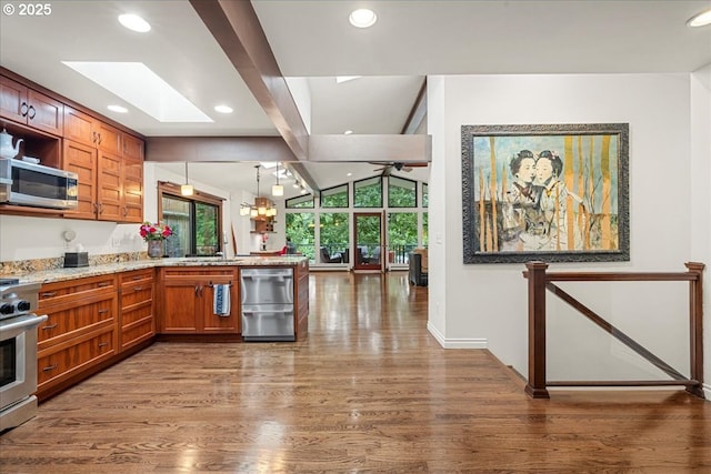 kitchen featuring appliances with stainless steel finishes, a peninsula, wood finished floors, a skylight, and recessed lighting