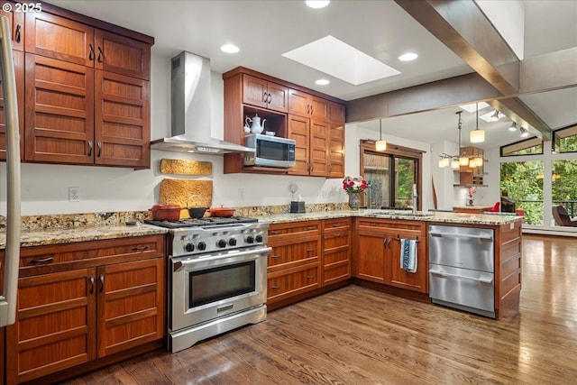 kitchen featuring appliances with stainless steel finishes, wall chimney exhaust hood, a peninsula, a sink, and a skylight