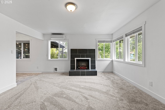 unfurnished living room featuring a wall mounted AC, carpet floors, a tiled fireplace, and baseboards