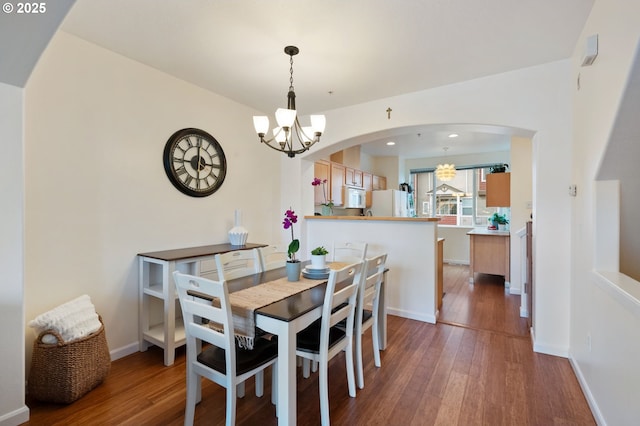 dining space featuring dark wood-style floors, arched walkways, baseboards, and an inviting chandelier