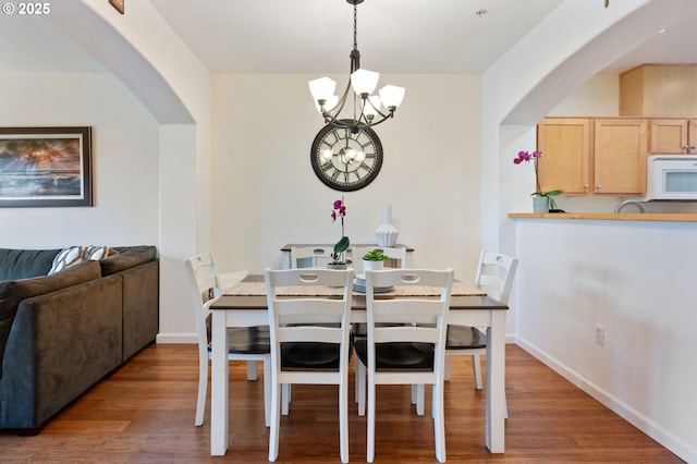 dining area featuring a chandelier, arched walkways, baseboards, and wood finished floors