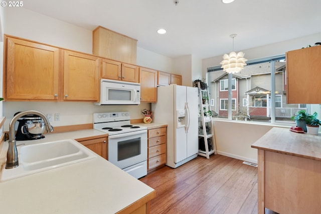 kitchen featuring white appliances, hanging light fixtures, light countertops, light wood-type flooring, and light brown cabinets