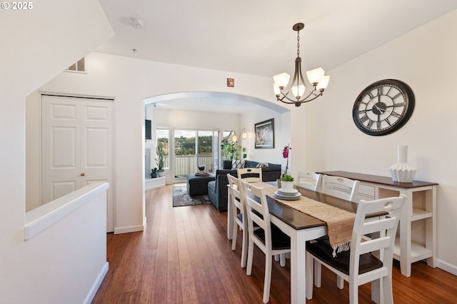 dining space with arched walkways, dark wood-style flooring, visible vents, an inviting chandelier, and baseboards