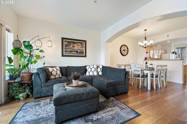 living room featuring baseboards, a chandelier, arched walkways, and wood finished floors