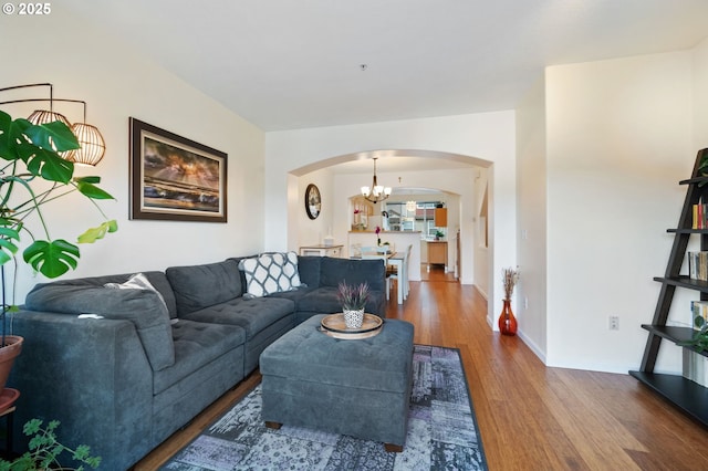 living area with arched walkways, baseboards, an inviting chandelier, and wood finished floors