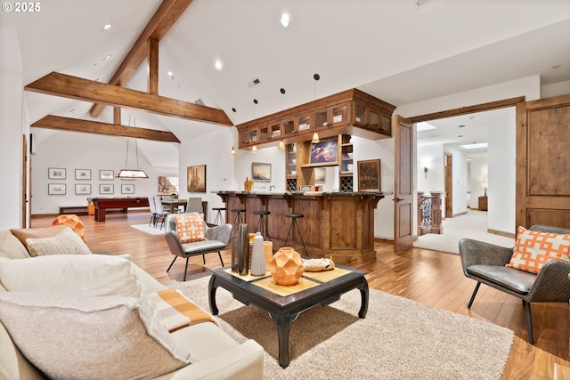 living room with bar, beamed ceiling, high vaulted ceiling, and light wood-type flooring