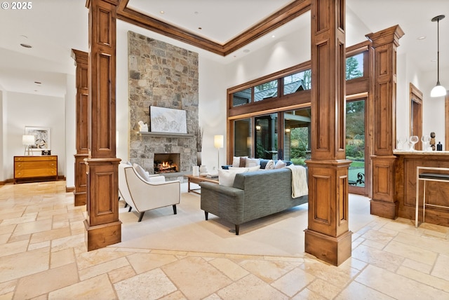 living room featuring a high ceiling, decorative columns, a stone fireplace, and crown molding