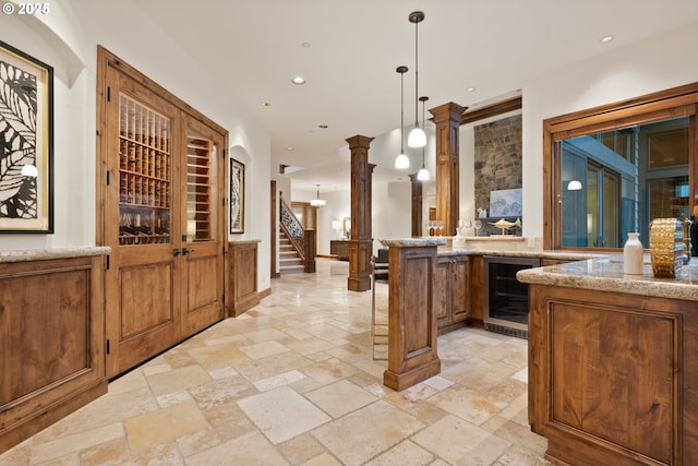 bar featuring light stone countertops, decorative light fixtures, wine cooler, and decorative columns