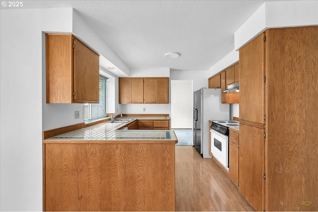 5868 NW Landing Dr, Portland, OR 97210 - kitchen with white electric range, under cabinet range hood, brown cabinets, light wood finished floors, and a textured ceiling