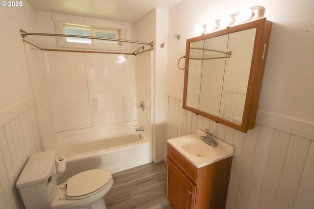 bathroom with toilet, wainscoting, wood finished floors, vanity, and  shower combination