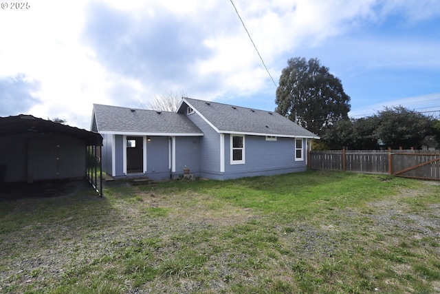 back of house featuring an outbuilding, a lawn, a shed, fence, and a shingled roof