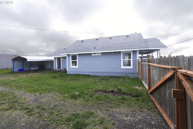 back of property featuring a lawn, a shingled roof, and fence