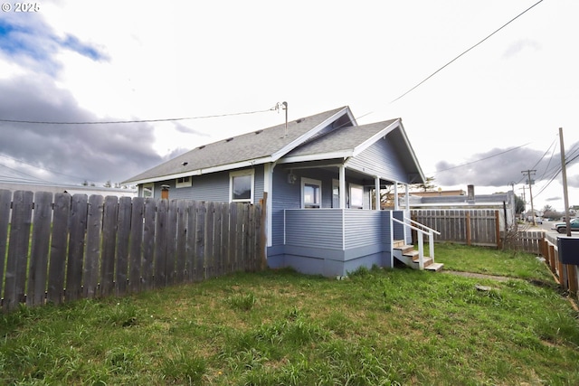 rear view of property featuring a porch, a lawn, fence, and roof with shingles