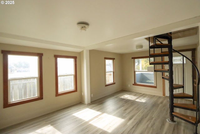 unfurnished living room featuring light wood-type flooring, baseboards, and stairs