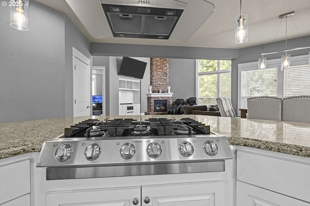 2021 Pikes Pass Ct, Salem, OR 97306 - kitchen featuring stainless steel gas stovetop, white cabinetry, light stone countertops, exhaust hood, and a stone fireplace