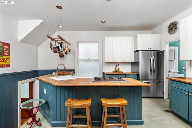 kitchen with a wainscoted wall, butcher block counters, appliances with stainless steel finishes, white cabinetry, and a sink