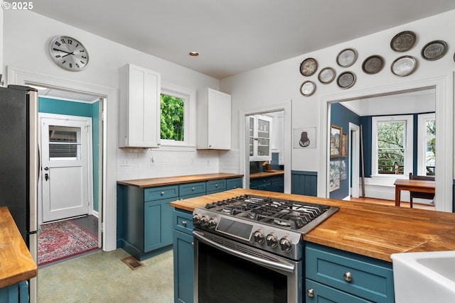 kitchen with backsplash, blue cabinetry, butcher block countertops, white cabinets, and stainless steel appliances