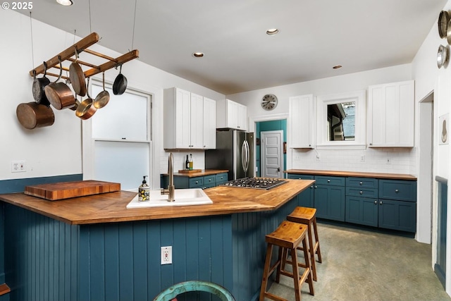 kitchen with blue cabinets, a sink, backsplash, appliances with stainless steel finishes, and wooden counters