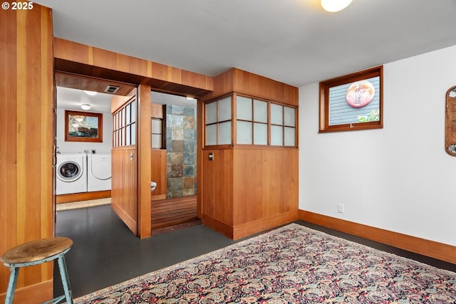 interior space with visible vents, baseboards, concrete floors, wood walls, and washer and clothes dryer