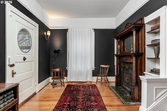 entrance foyer with baseboards, a fireplace with raised hearth, and light wood finished floors