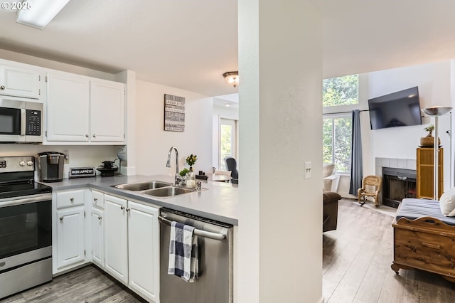 kitchen featuring white cabinets, a tile fireplace, a sink, light wood-style flooring, and stainless steel appliances