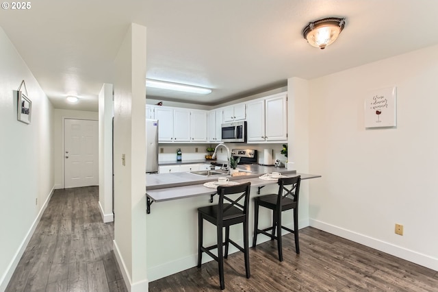 17532 NW Springville Rd Unit D8, Portland, OR 97229 - kitchen with appliances with stainless steel finishes, dark wood-type flooring, a peninsula, white cabinetry, and a kitchen bar