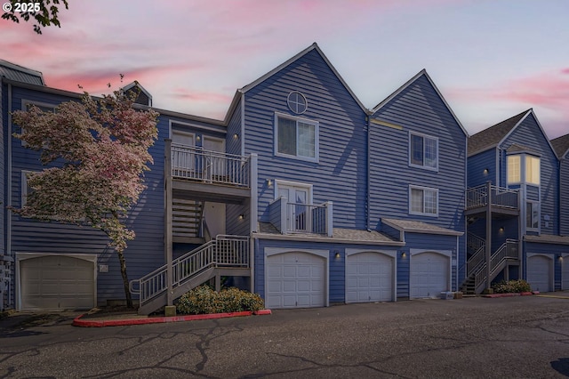 townhome / multi-family property featuring stairway, an attached garage, a balcony, and aphalt driveway