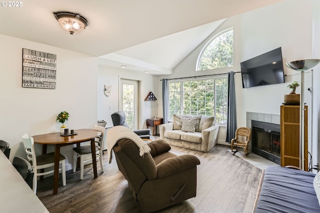 living area featuring high vaulted ceiling, a tiled fireplace, and wood finished floors