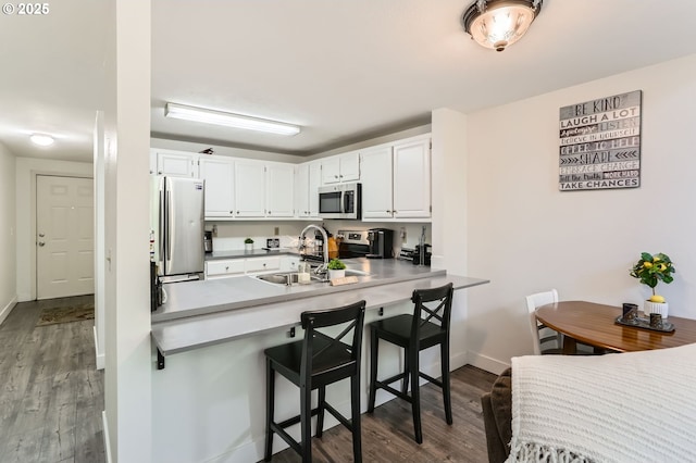 kitchen with wood finished floors, a sink, white cabinets, a peninsula, and stainless steel appliances