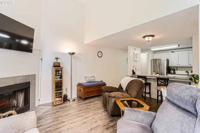living room featuring light wood-style floors, a high ceiling, and a tile fireplace