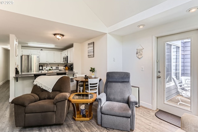 living area with baseboards, lofted ceiling, and light wood-type flooring