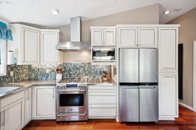 kitchen with wall chimney range hood, stainless steel countertops, white cabinets, lofted ceiling, and stainless steel appliances