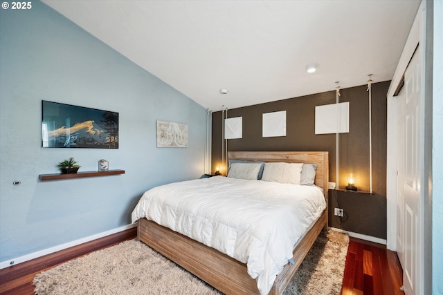 bedroom with baseboards, lofted ceiling, and wood finished floors