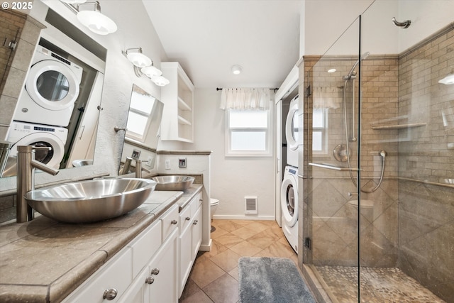full bathroom featuring stacked washer and clothes dryer, a shower stall, toilet, and visible vents