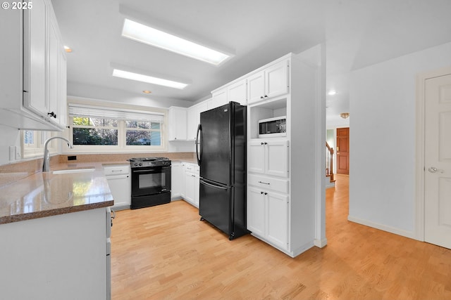 kitchen with sink, black appliances, light hardwood / wood-style flooring, dark stone counters, and white cabinets