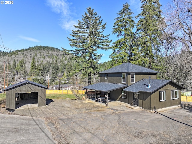 view of front of home with a view of trees, roof with shingles, a detached garage, and fence