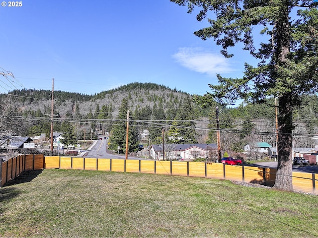 view of yard featuring a mountain view, a view of trees, and fence