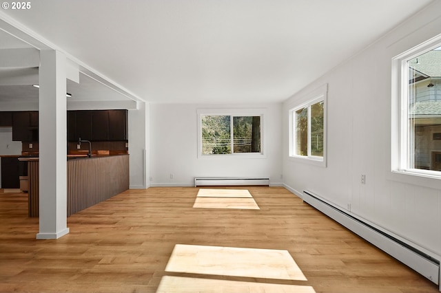 unfurnished room featuring a sink, a baseboard heating unit, and light wood-style floors