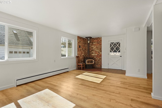 interior space with light wood-style flooring, baseboards, a wood stove, and a baseboard radiator