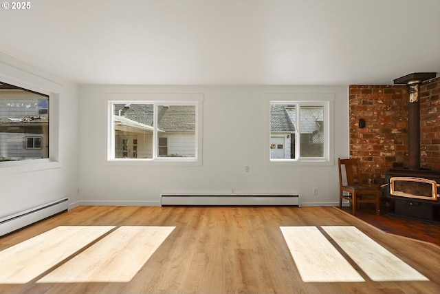 unfurnished living room with baseboard heating, a wood stove, baseboards, and wood finished floors