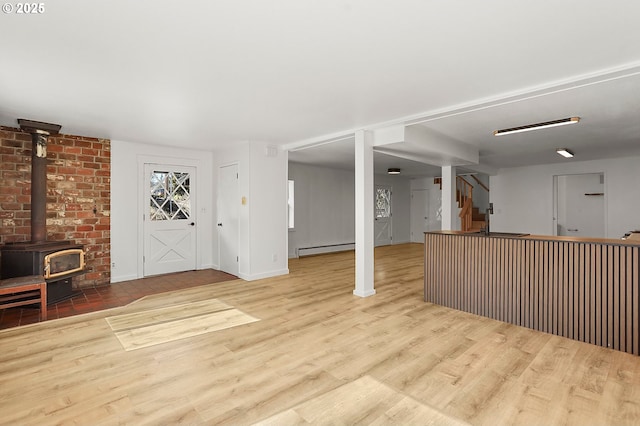 unfurnished living room with baseboards, stairs, a wood stove, wood finished floors, and a baseboard radiator