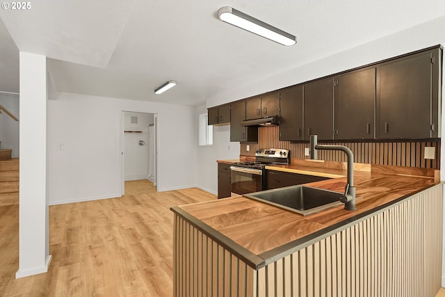 kitchen featuring dark brown cabinets, under cabinet range hood, light wood-type flooring, stainless steel electric range, and a sink