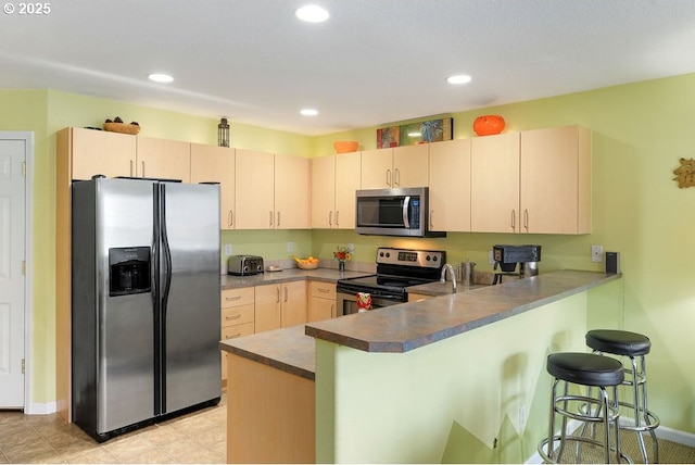 kitchen with light brown cabinets, appliances with stainless steel finishes, kitchen peninsula, and a breakfast bar area